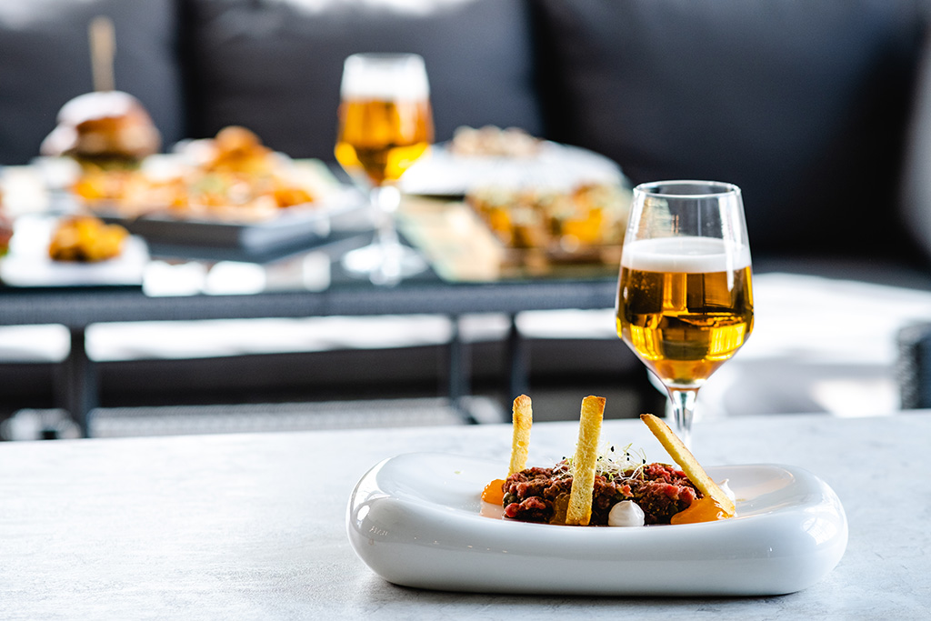 Tartar serviert auf einem Gourmet-weißen Teller neben einem Glas Premium-Bier