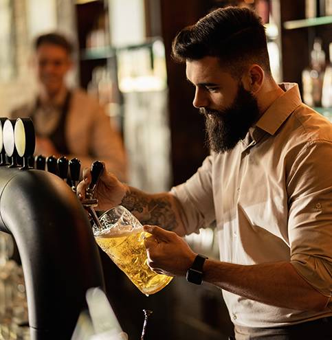 Young barista working a bar counter and pouring beer from a beer tap.