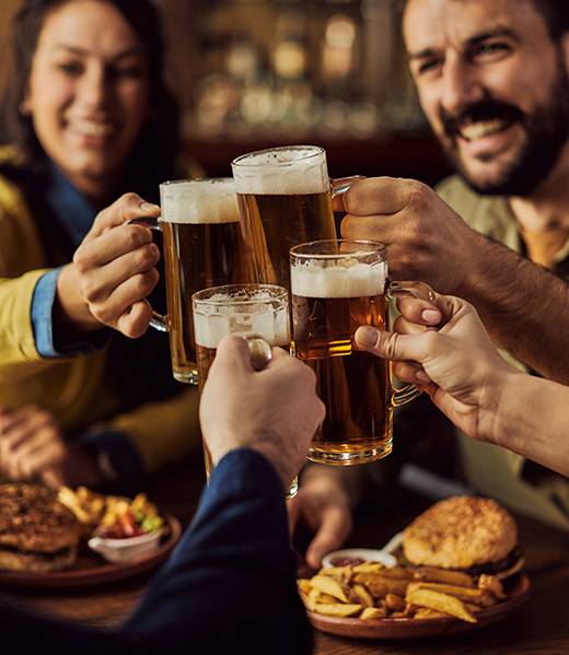 Close-up of group of friends toasting with beer while eating in a pub.